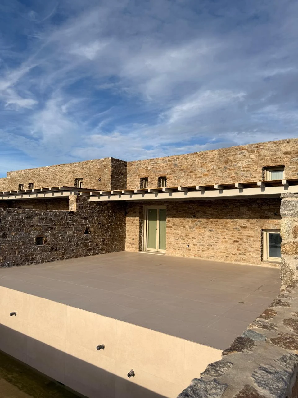 Paragka, Mykonos · Wide terrace framed by a stone facade and timber pergola.