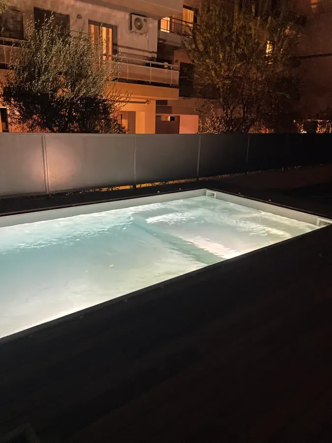 Φωτισμένη υπαίθρια πισίνα δίπλα σε τοίχο κήπου τη νύχτα